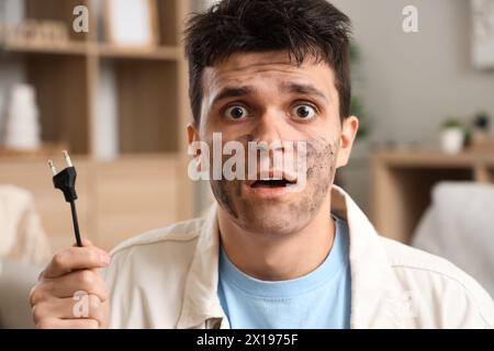 Ein Mann mit einem Stromschlag, verbranntem Gesicht und Stecker zu Hause, Nahaufnahme Stockfoto