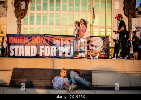 Tel Aviv, Israel. April 2024. Ein israelisches Paar sitzt unter einem Banner und ruft US-Präsident Joe Biden dazu auf, den israelischen Premierminister Benjamin Netanjahu während einer Demonstration daran zu hindern, den Iran anzugreifen. Israel hat nach einem beispiellosen Drohnen- und Raketenangriff am Wochenende, der die regionalen Spannungen, die durch den Krieg in Gaza geschürt wurden, verschärft hat, gelobt, vom Iran einen "Preis" abzugeben. (Foto von Eyal Warshavsky/ SOPA Images/SIPA USA) Credit: SIPA USA/Alamy Live News Stockfoto