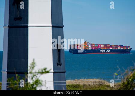 Cape Henry, Virginia, USA – 13. April 2024: Ein Hapag-Lloyd-Frachtschiff fährt am „neuen“ Cape Henry Lighthouse am Eingang zur Chesapeake Bay vorbei. Stockfoto