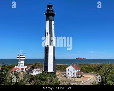 Cape Henry, Virginia, USA – 13. April 2024: Ein Hapag-Lloyd-Containerschiff, das in der Ferne am „neuen“ Cape Henry Lighthouse und Kontrollturm vorbeigesehen wird. Stockfoto