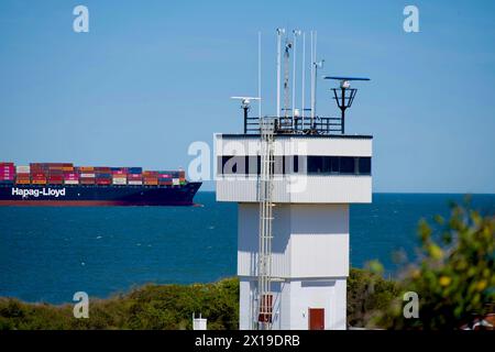 Cape Henry, Virginia, USA – 13. April 2024: Ein Hapag-Lloyd-Frachtschiff segelt hinter dem Kontrollturm am südlichen Eingang der Chesapeake Bay. Stockfoto