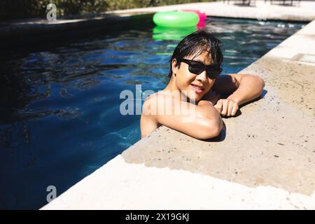 Ein Teenager asiatischer Junge, der sich zu Hause im Pool entspannt, Sonnenbrille trägt, Kopierraum Stockfoto