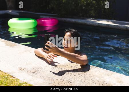 Ein asiatischer Teenager, der draußen am Pool Selfie macht, ohne Hemd Stockfoto