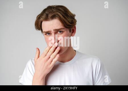 Junger Mann mit Hand über Mund, der Anzeichen von Bedauern oder Schock zeigt Stockfoto