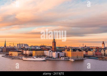 Goldener orangefarbener Sonnenuntergang über der Altstadt von Stockholm und der Riddarholmen-Kirche. Cirrus Wolken beleuchtet von der Sonne. Farbenfrohe historische Gebäude. Stockfoto