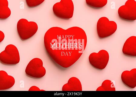 Alles Gute zum Muttertag. Draufsicht des roten Herzens mit dem Text Happy Mothers Day und viele kleine rote Herzen auf rosa Hintergrund Stockfoto