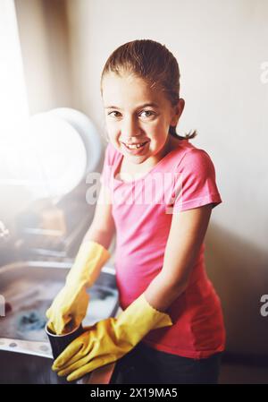 Porträt, Geschirr waschen oder Kind mit schmutziger Tasse oder Handschuhen in Küchenspüle zu Hause für gesunde Hygiene. Glücklich, Entwicklung oder Mädchen putzen mit Seife Stockfoto