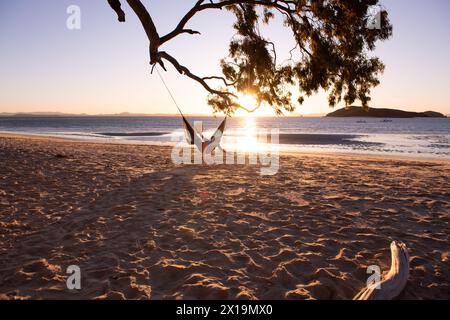 Weiblich, die sich in einer Hängematte von einem Baum an einem tropischen Strand entspannen Stockfoto