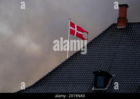 Kopenhagen, Dänemark. April 2024. Rauch umgibt die dänische Flagge über dem Finanzministerium neben dem historischen Gebäude Boersen, das am Dienstag, den 16. April 2024, im Zentrum Kopenhagens in Dänemark in Brand steht. In dem Gebäude, das gerade renoviert wird, brach am Dienstagmorgen ein heftiges Feuer aus. Das Gebäude wurde in den 1620er Jahren als Geschäftshaus von König Christian IV. Errichtet und befindet sich neben dem dänischen parlament. Kredit: Ritzau/Alamy Live News Kredit: Ritzau/Alamy Live News Stockfoto