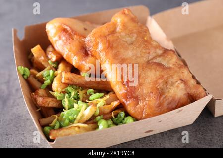 Leckerer Fisch, Chips und Erbsen in Papierkarton auf grauem Tisch, Nahaufnahme Stockfoto