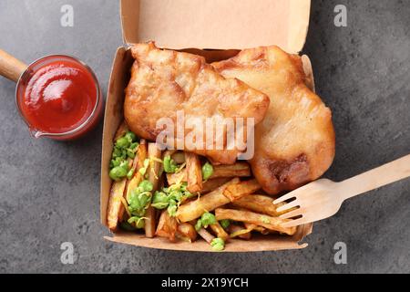 Leckerer Fisch, Chips, Soße und Erbsen in Papierkarton auf grauem Tisch, Blick von oben Stockfoto