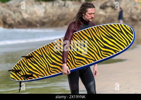 Ein müder Surfer mit seinem unverwechselbaren Surfbrett nach einer Surfsession in Fistral in Newquay in Cornwall in Großbritannien. Stockfoto