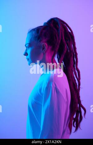 Vertikales Seitenporträt einer kaukasischen jungen Frau mit langen Dreadlocks im blauen und lila Neonlicht Stockfoto