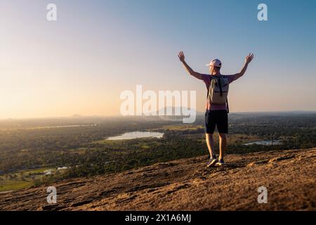 Rückansicht eines Mannes mit Rucksack, der den Sonnenuntergang genießt. Glücklicher Alleinreisender mit erhobenen Armen in Sri Lanka. Stockfoto