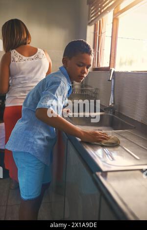 Junge, Kind und Reinigung auf Waschbecken in der Küche mit Mutter für Keime, Hygiene und Hauspflege. Sohn, Kind und Tuch mit Wischtuch auf der Theke für Stockfoto