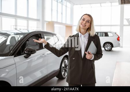 Lächelnde Verkäuferin, die einen Tablet-PC hält, während sie die Kamera im Ausstellungsraum eines neuen Autos betrachtet Stockfoto