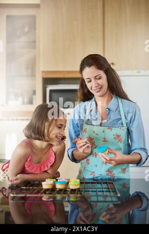 Mutter, Kind und Cupcakes, die zu Hause backen oder Dessert als Deko, Lernen oder Binden. Frau, Tochter und Lehrer an der Küchentheke für Stockfoto