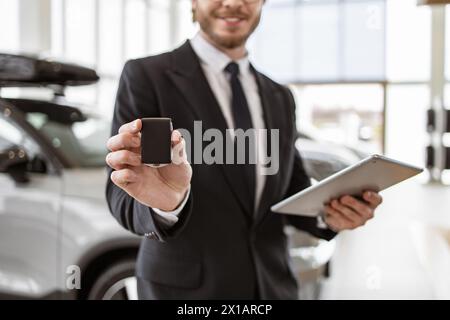 Selektive Fokussierung auf Schlüssel in der Hand eines Kaukasiers-Autohändlers. Autoverkäufer lächelt fröhlich, hält Schlüssel und steht vor neuen Fahrzeugen für sal Stockfoto