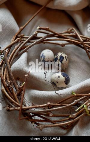 Drei Wachteleier sind in einem Weihnachtsschmuck aus natürlichen Materialien, darunter Äste und Zweige, eingebettet, die einem Kranz ähneln Stockfoto