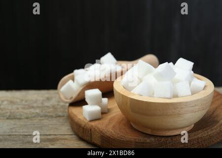 Weiße Zuckerwürfel in Schüssel und Schaufel auf Holztisch vor dunklem Hintergrund, Nahaufnahme. Leerzeichen für Text Stockfoto