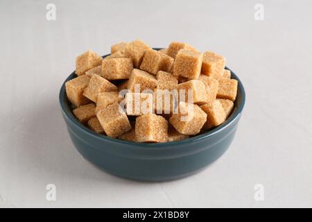 Braune Zuckerwürfel in der Schüssel auf einem leicht strukturierten Tisch Stockfoto