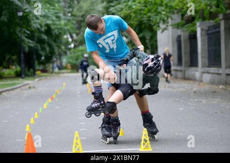 Rollerblading. Trainer, der mit dem kleinen Jungen herumspielt, während er ihm künstlerischen Slalom beibrachte. Juni 2019. Kiew, Ukraine Stockfoto