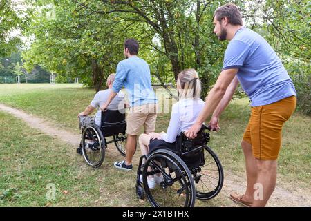 Eine herzerwärmende Szene mit vier Freunden, darunter zwei mit Rollstühlen, die gemeinsam in einem üppig grünen Park Zeit verbringen. Stockfoto