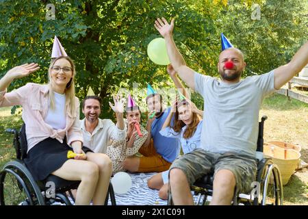 Gruppe glücklicher Freunde, die eine Party im Park feiern, wobei eine Person, die einen Rollstuhl benutzt, aktiv teilnimmt und lächelt. Stockfoto