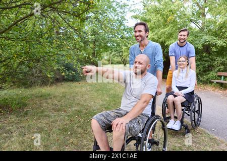 Eine vielfältige und fröhliche Gruppe von Menschen, einschließlich Personen im Rollstuhl, die einen Moment des Glücks und der Freundschaft im Freien in einem Park teilen. Stockfoto