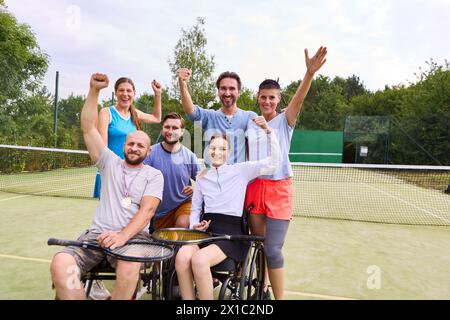 Eine vielfältige Gruppe von Freunden, darunter eine Person, die einen Rollstuhl benutzt und einen Sieg auf einem Tennisplatz feiert. Stockfoto