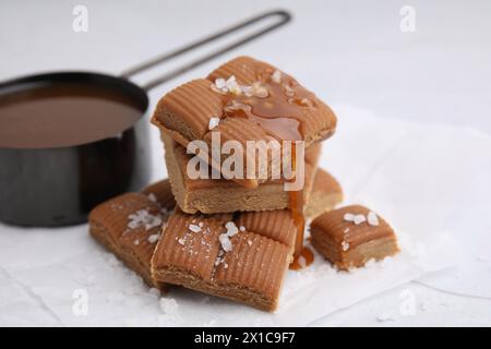 Leckere Karamellbonbons, Soße und Meersalz auf weißem Tisch, Nahaufnahme Stockfoto