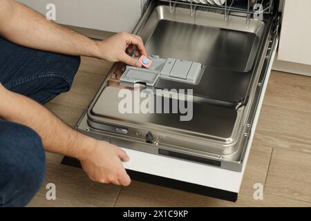 Mann, der Waschmitteltablette in den offenen Geschirrspüler steckt, Nahaufnahme Stockfoto