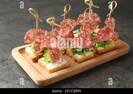 Leckere Kanapees mit Salami, Gemüse und Frischkäse auf grauem Tisch Stockfoto