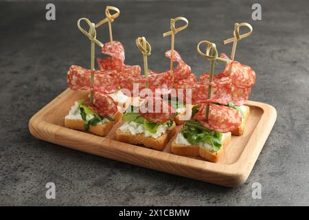 Leckere Kanapees mit Salami, Gemüse und Frischkäse auf grauem Tisch Stockfoto