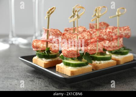 Leckere Kanapees mit Salami, Gurke und Frischkäse auf grauem Tisch, Nahaufnahme Stockfoto