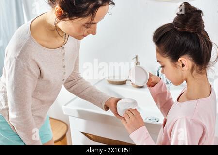 Eine brünette Frau hilft ihrer jungen Tochter liebevoll in einem modernen Badezimmer während ihrer Schönheits- und Hygienearbeit. Stockfoto