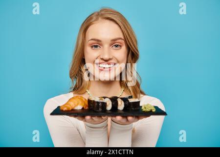 Eine schöne blonde Frau hält zart einen Teller frisch zubereitetes Sushi. Stockfoto
