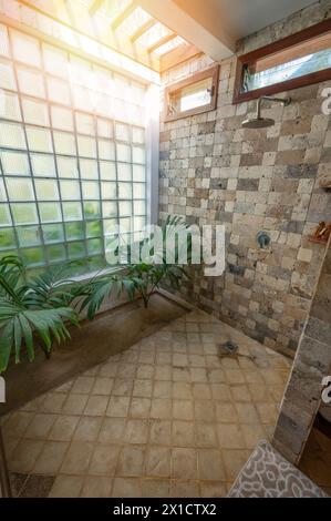 Bad mit Naturstein, Dusche mit großem Fenster und grünen Pflanzen Stockfoto