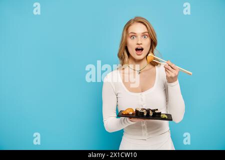 Die ansprechende Frau hält elegant ein Tablett mit Sushi und Essstäbchen und zeigt ihr kulinarisches Know-how mit einem Hauch von Raffinesse. Stockfoto