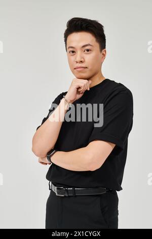 Ein modischer junger Mann in eleganter Kleidung posiert selbstbewusst für eine Kamera in einem schwarzen Hemd. Stockfoto
