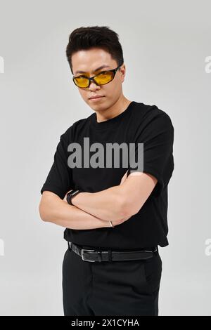Ein modischer junger Mann mit überkreuzten Armen und Sonnenbrille zeigt sich selbstbewusst in eleganter Kleidung. Stockfoto