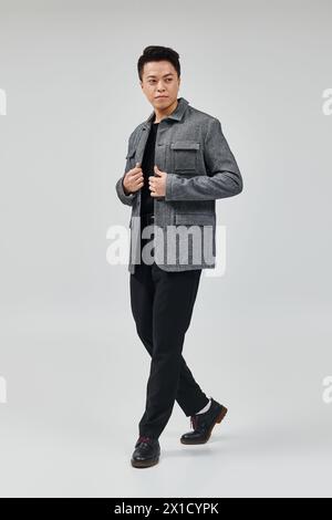 Ein modischer junger Mann in grauer Jacke und schwarzer Hose, der eine dynamische Pose zeigt. Stockfoto