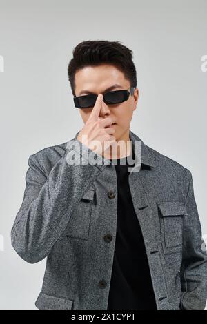 Ein modischer junger Mann posiert selbstbewusst in einer stilvollen grauen Jacke und einer trendigen Sonnenbrille. Stockfoto