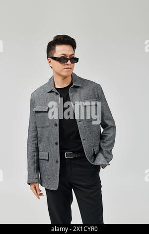 Ein modischer junger Mann posiert selbstbewusst in einer grauen Jacke und einer schwarzen Hose. Stockfoto
