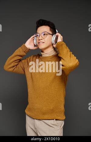 Ein stilvoller Mann in braunem Pullover und einer Brille hört Musik über Kopfhörer. Stockfoto