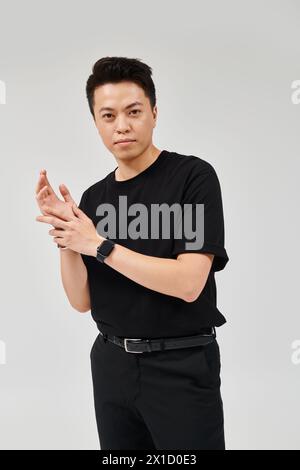 Ein modischer junger Mann posiert selbstbewusst in einem schwarzen Hemd und einer schwarzen Hose und strahlt Eleganz und Stil aus. Stockfoto