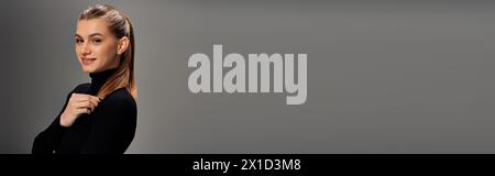 Eine junge Frau mit langen Haaren posiert vor grauem Hintergrund, strahlt Selbstvertrauen und Anmut aus, Banner Stockfoto