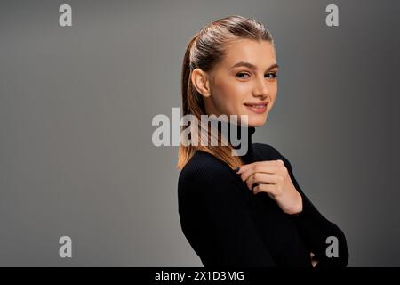 Eine junge, fröhliche Frau strahlt Eleganz in einem schwarzen Pullover aus, ihr langes Haar zieht sich über die Schulter. Stockfoto