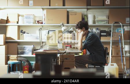 Zielgerichteter, intelligenter Teenager, der am Schreibtisch in seiner Garage sitzt und mit einem alten Computer arbeitet Stockfoto