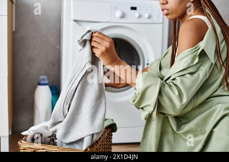 Eine afroamerikanische Frau mit Afro-Zöpfen wird gesehen, wie sie ihre Kleidung in einem Wäschekorb im Badezimmer trocknet. Stockfoto